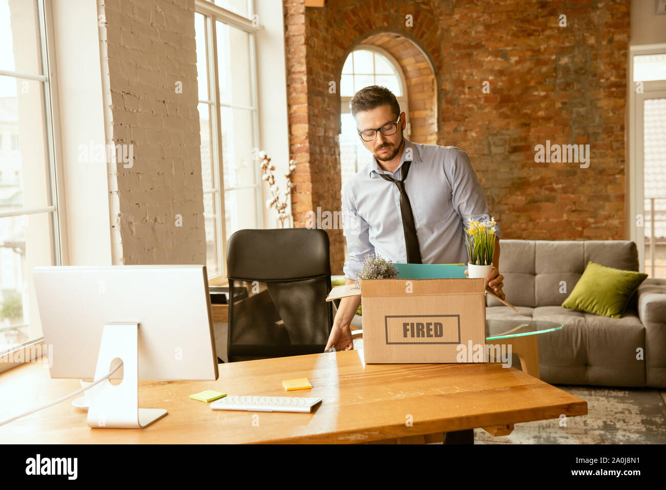 Junge Unternehmer abgefeuert, traurig aussieht. Hat sein Büro Sachen zu packen und Arbeitsplatz für neue Arbeitnehmer zu verlassen. Probleme im Beruf, Stress, Arbeitslosigkeit, ein neuer Weg des Lebens oder am Ende der Karriere. Stockfoto