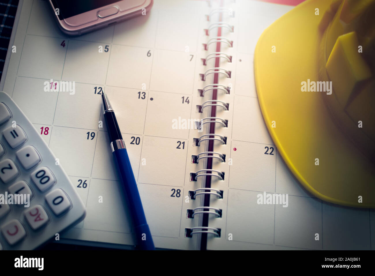 Notebook Kalender mit Kugelschreiber, Handy, Taschenrechner und Bau Helm auf dem Schreibtisch unter Licht. Stockfoto