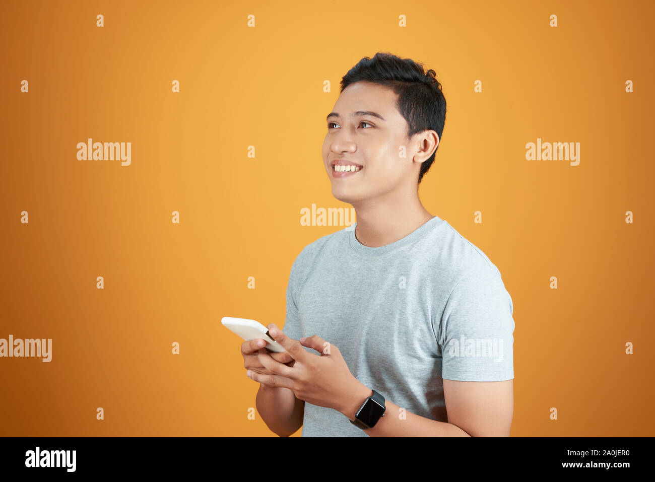 Smart Casual asiatischer Mann mit Smartphone in orange hinterlegt. Stockfoto
