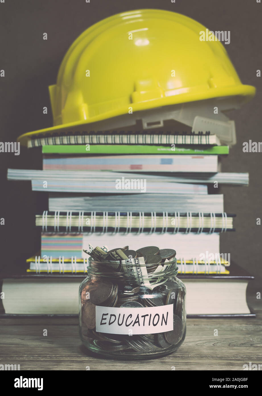 Sparen Sie bares Geld für die Ausbildung in den Glasbehälter mit Heap der Buch- und Bau Helm Stockfoto