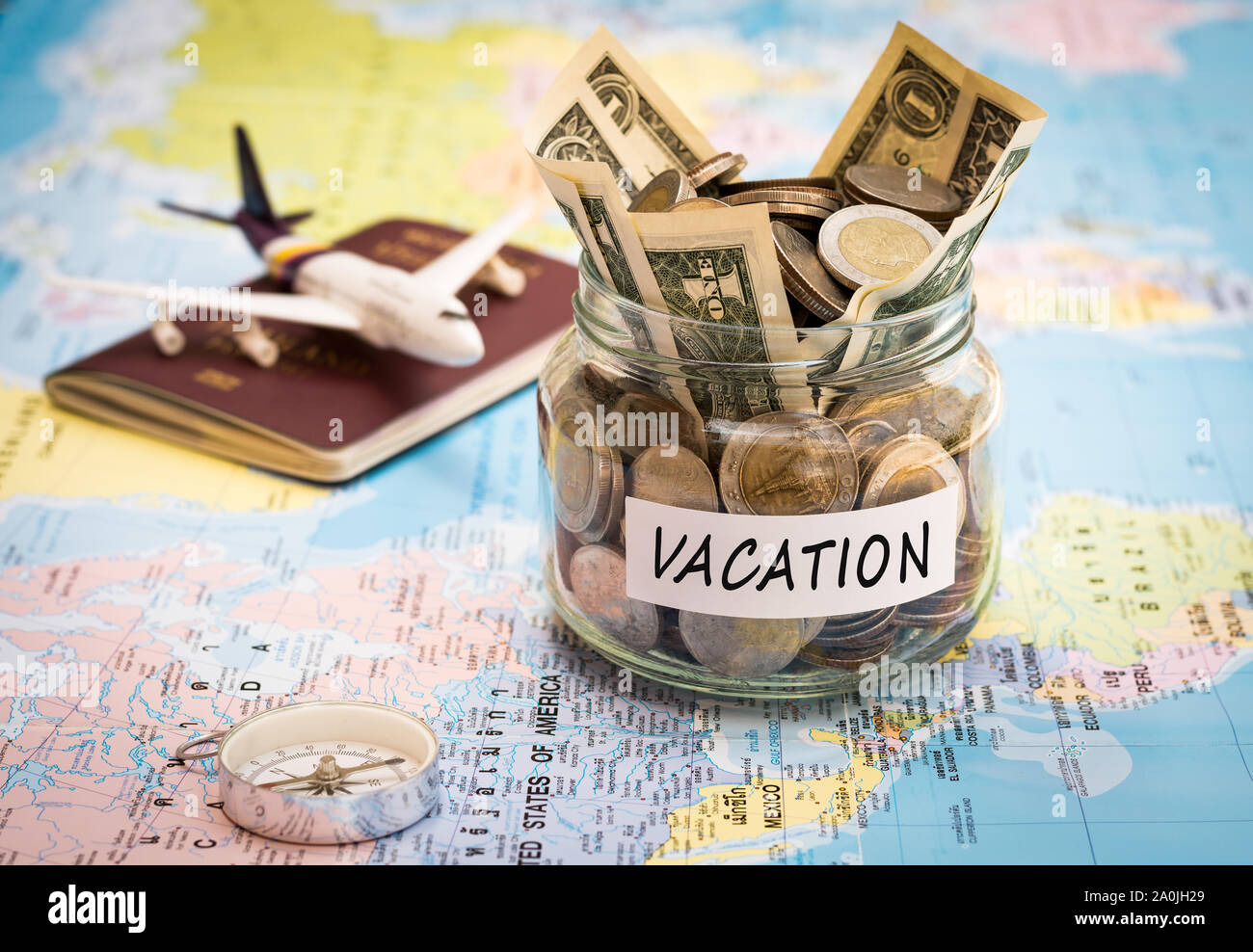 Urlaub Haushalt Konzept. Urlaub Geld zu sparen, in einem Glas mit Kompass, Reisepass und Flugzeuge Spielzeug auf Weltkarte Stockfoto