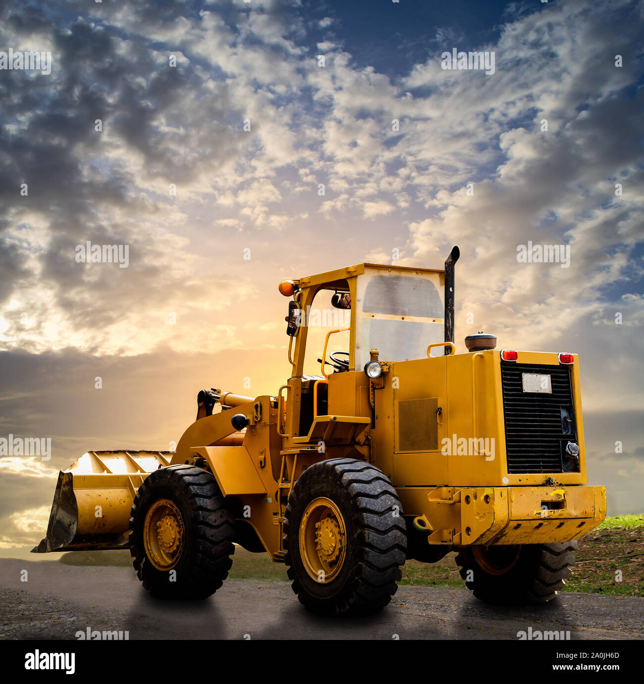 Gelbe Traktor auf der Straße mit bewölkt blauer Himmel Stockfoto