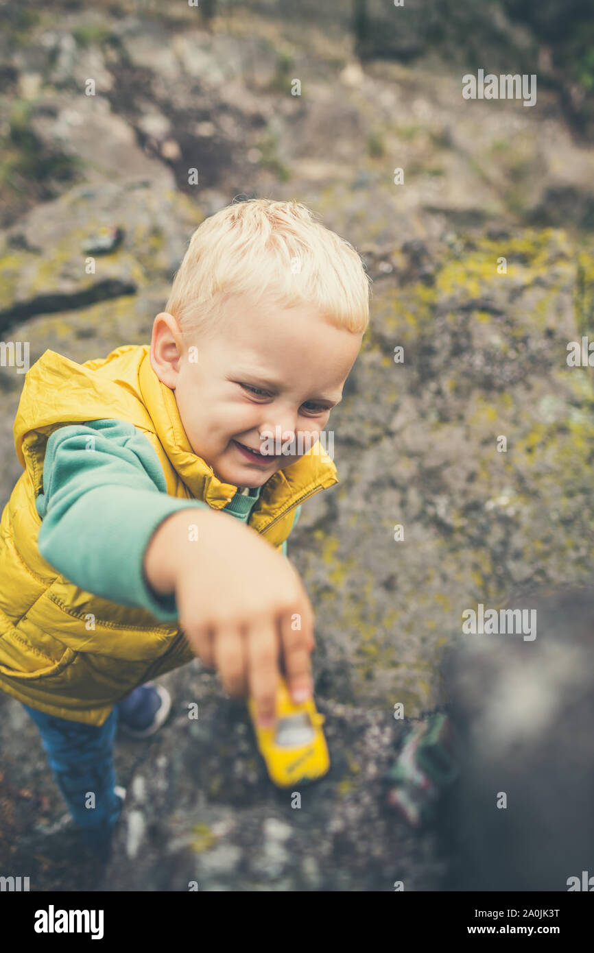 Toddler Boy mit Spielzeug spielen auf einem Felsen. Kleines Kind zu Fuß auf Rocky Mountains. Stockfoto