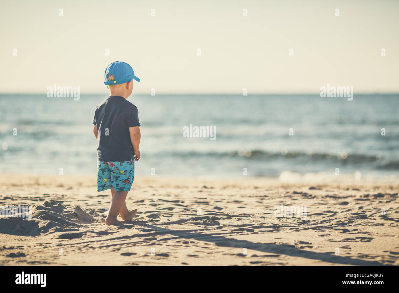 Toddler boy zu Fuß auf einem sonnigen Strand. Kleines Kind gehen auf Sand. Schöne inspirierende Strand und Blick aufs Meer, Landschaft. Stockfoto