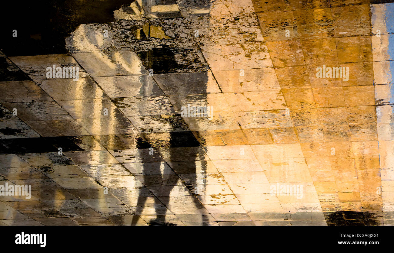 Blurry abstrakte Schatten silhouette Reflexionen von zwei Menschen zu Fuß auf nasser Straße Bürgersteig Stockfoto