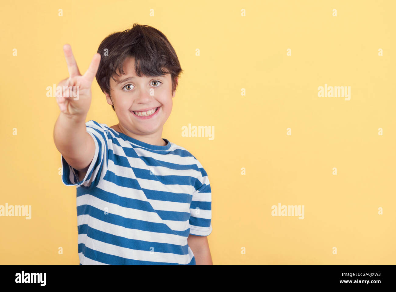 Kind lächelnd tun Sieg unterzeichnen. Nummer zwei auf gelbem Hintergrund Stockfoto