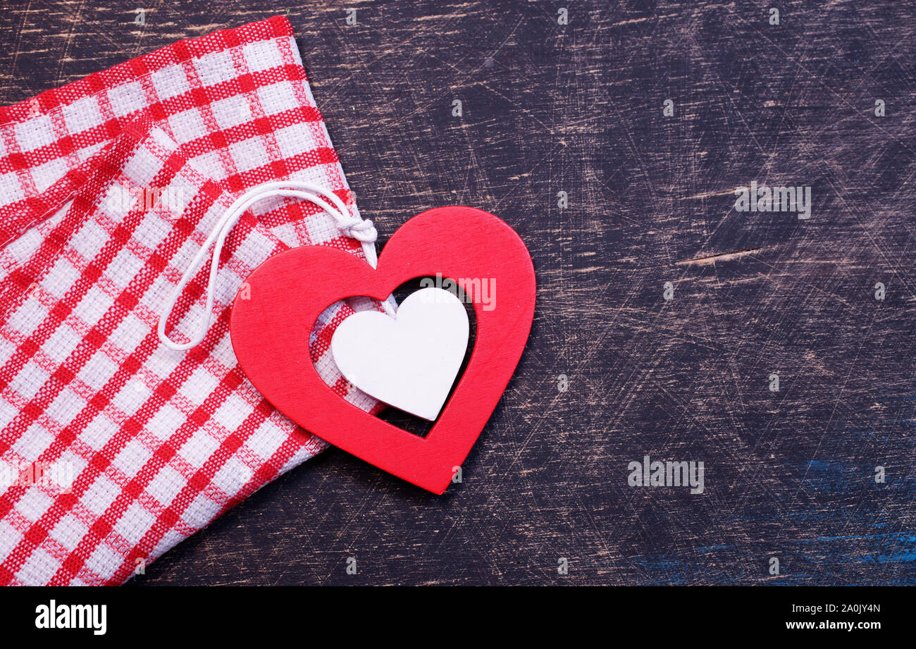 Rotes und weißes Holzherz auf einem schwarzen Tisch mit einem rot karierten Handtuch Stockfoto
