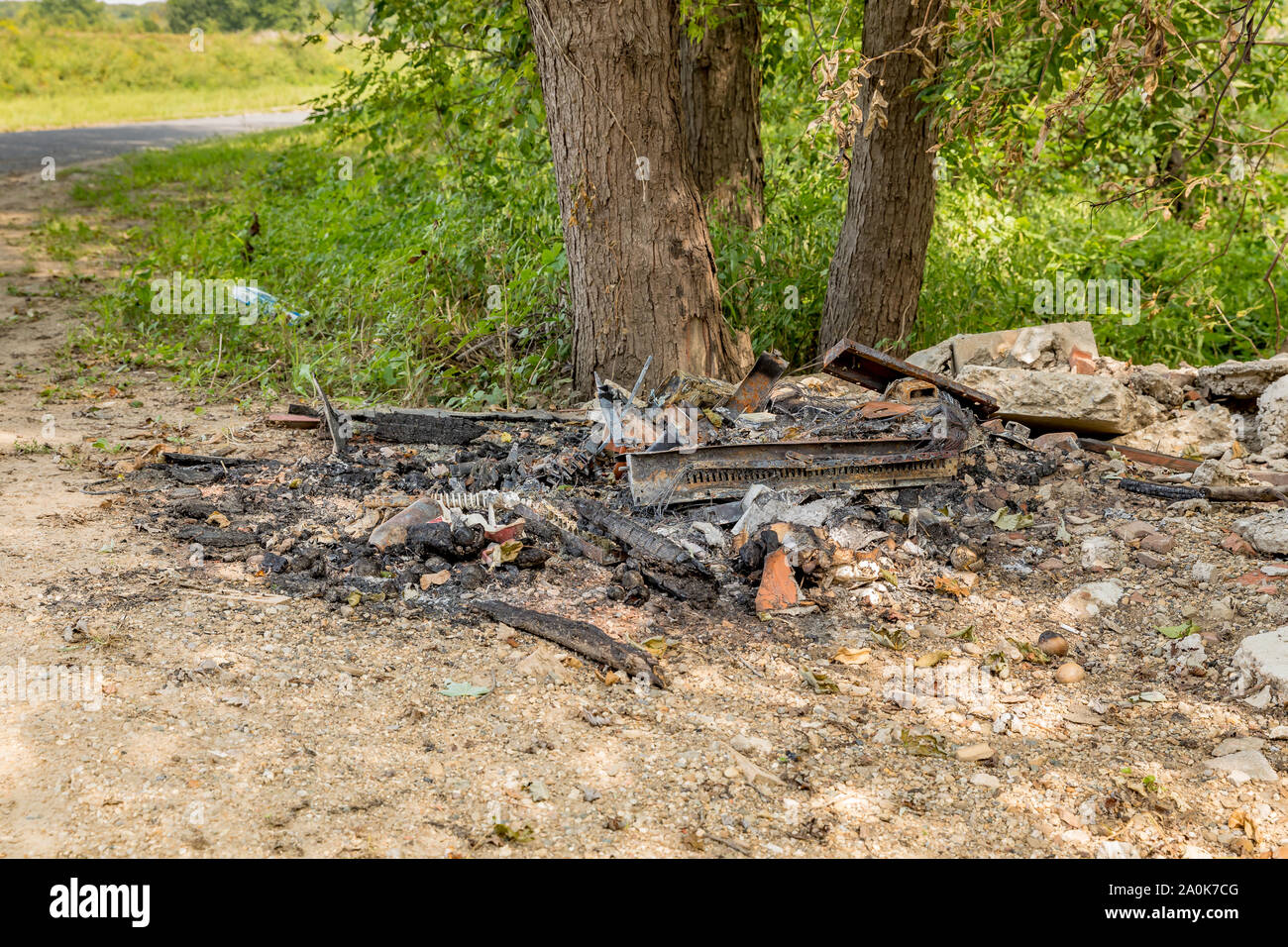 Abfall und Müll illegal entsorgt entlang einer Straße, die durch den Fluss und verbrannte, hinterlassen einen Haufen verkohlten Trümmern, Metall, und Kabel Stockfoto