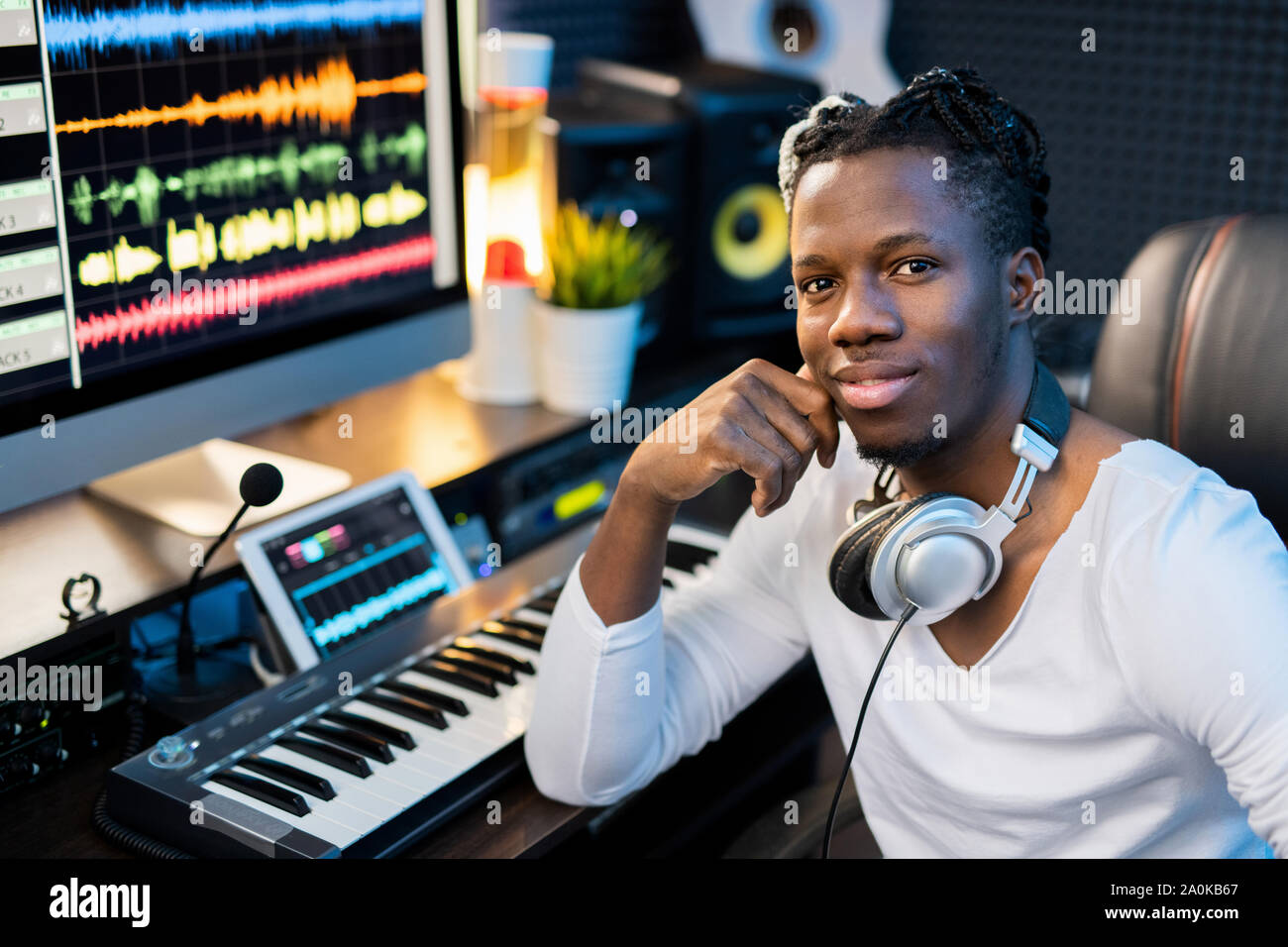 Glückliche junge lächelnd Mixed-race Mann mit Kopfhörer auf dem Hals durch Arbeitsplatz sitzen Stockfoto