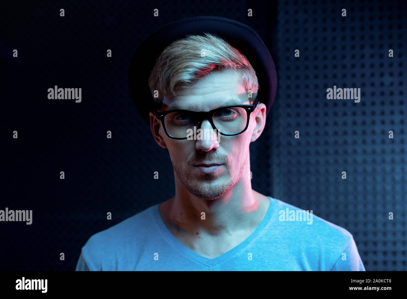 Ernster junger Mann in blauen pullover, schwarzen Hut und Brille im Studio Stockfoto