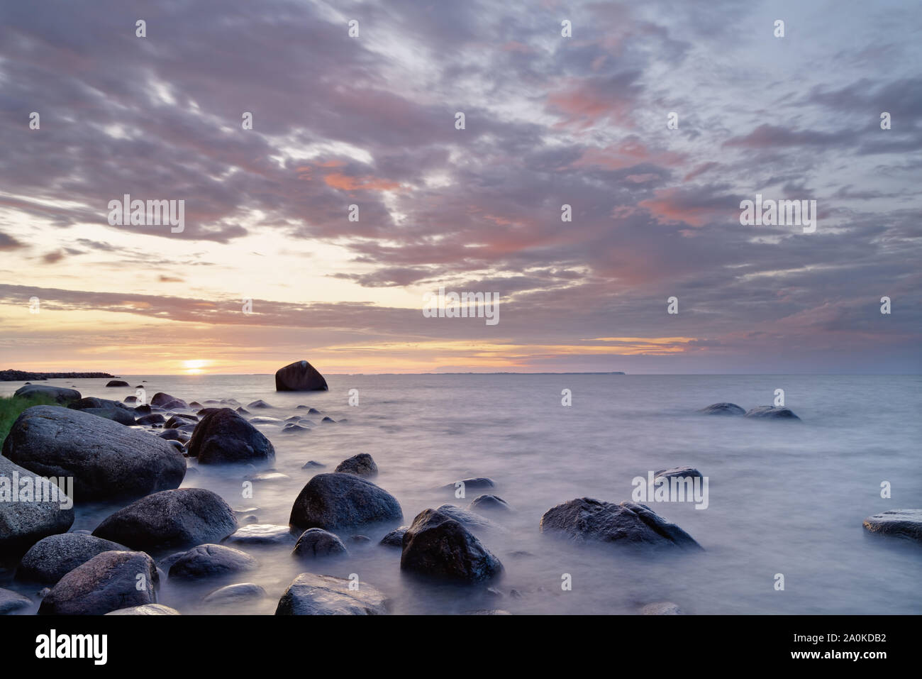 Große Steine am Strand der Ostsee im dramatischen Abend Licht für Sonnenuntergang mit roter Beleuchtung, Wolken, Wasser Bewegung in lange Belichtung - Ort: Stockfoto