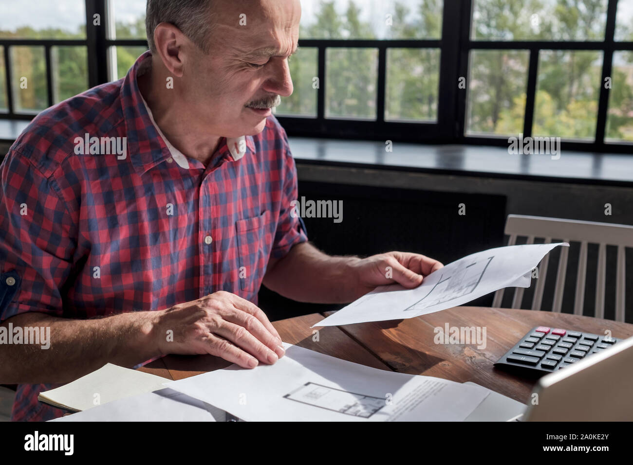 Senior Hispanic Mann mit Schnurrbart, die Pläne für die neue Wohnung zu entscheiden, was besser ist, zu kaufen. Hypothek im Alter. Kaufen Wohnung für Ihre Kinder Konzept. Stockfoto