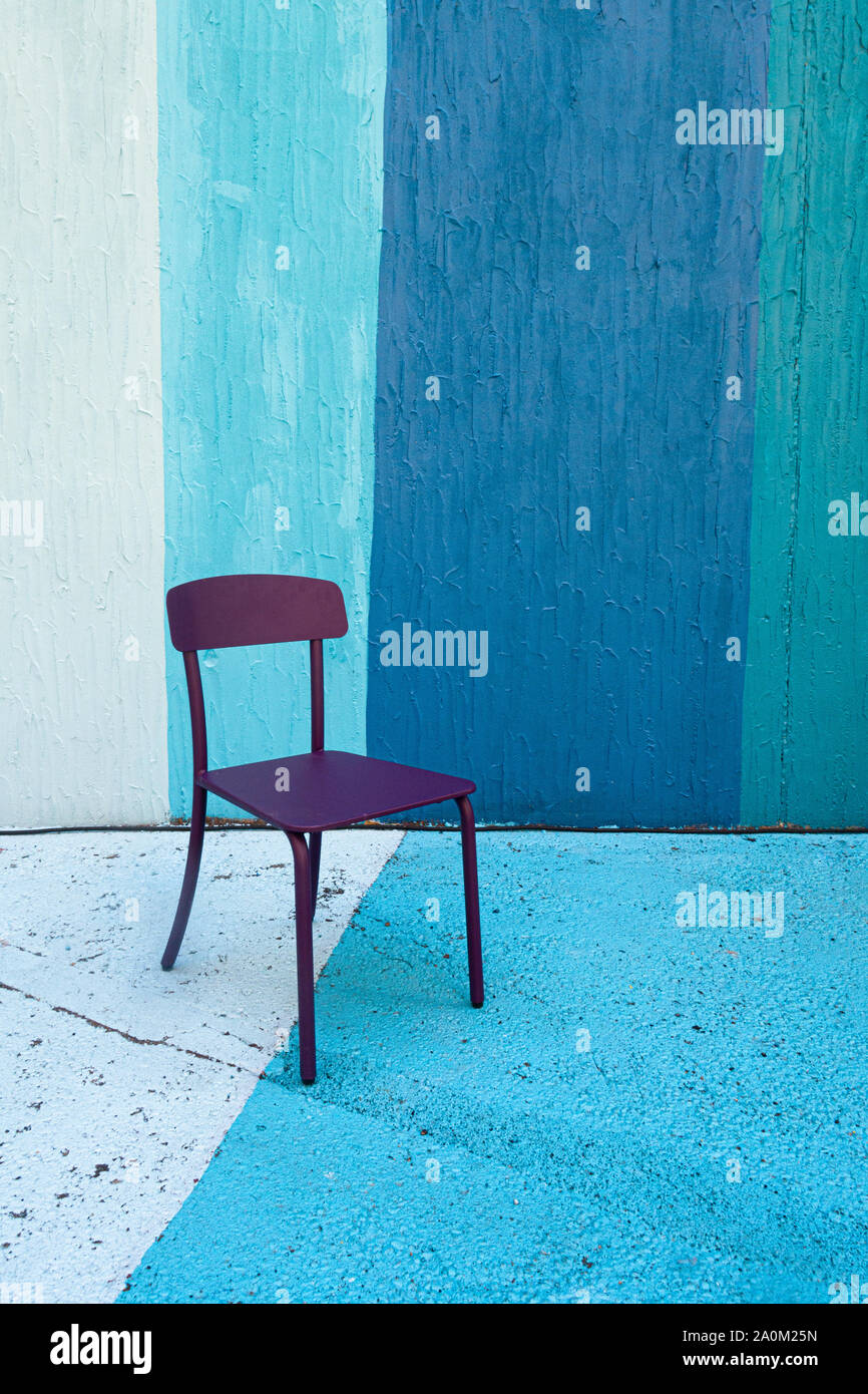 Ein einsamer, violetter Stuhl, der auf einem Hintergrund und einem Boden aus blau gestrichenen Streifen sitzt Stockfoto
