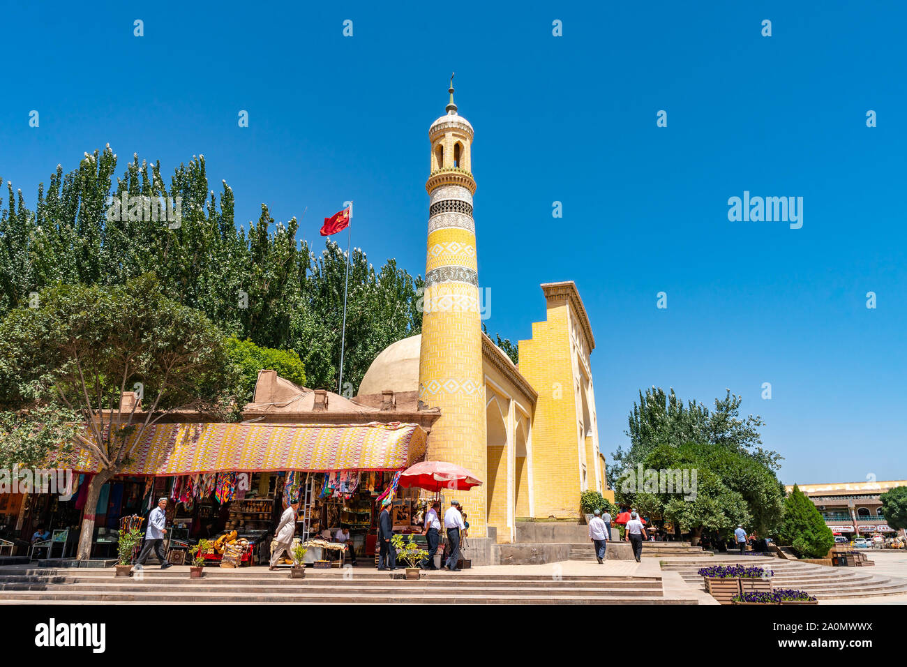 Kashgar Id kah-Moschee mit einem Winkenden China Flagge auf dem Dach und uigurische Männer mit Doppa Hut auf ihren Kopf auf einem sonnigen blauen Himmel Tag Stockfoto