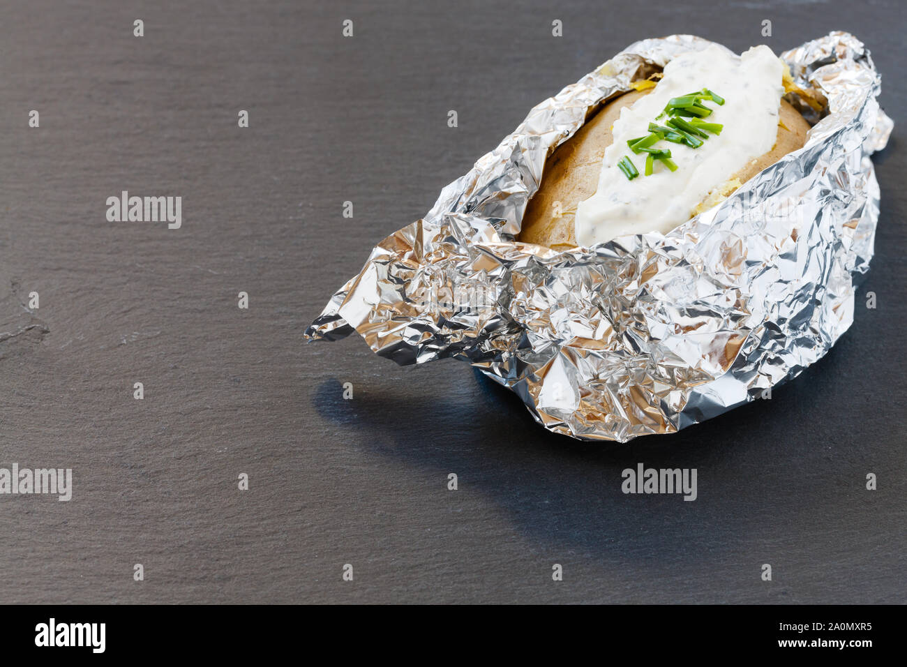 Ofen gebackene Kartoffeln in Alufolie mit Kräuter Frischkäse auf schiefer Board Stockfoto