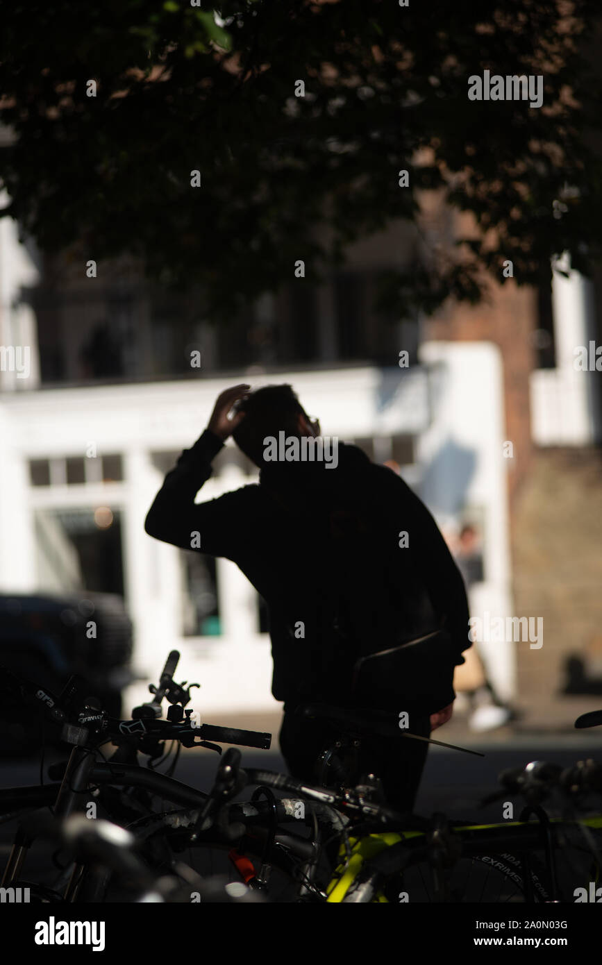 Ein junger Mann alter Anfang 30 geht weg vom Bike Rack, wo er sein Fahrrad verlassen hat. Silhouette. Aus Fokus Mann. Bike Rack ausgerichtet. Schatten Stockfoto