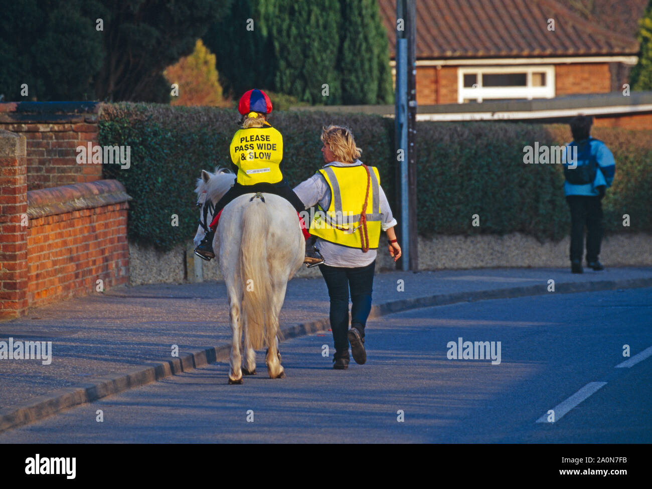 Pferd und Reiter unter der Leitung von Frau. Kind Reiter tragen Schärpe lesen "Bitte pass breit & langsam". Stalham, Norfolk, East Anglia, Großbritannien Stockfoto