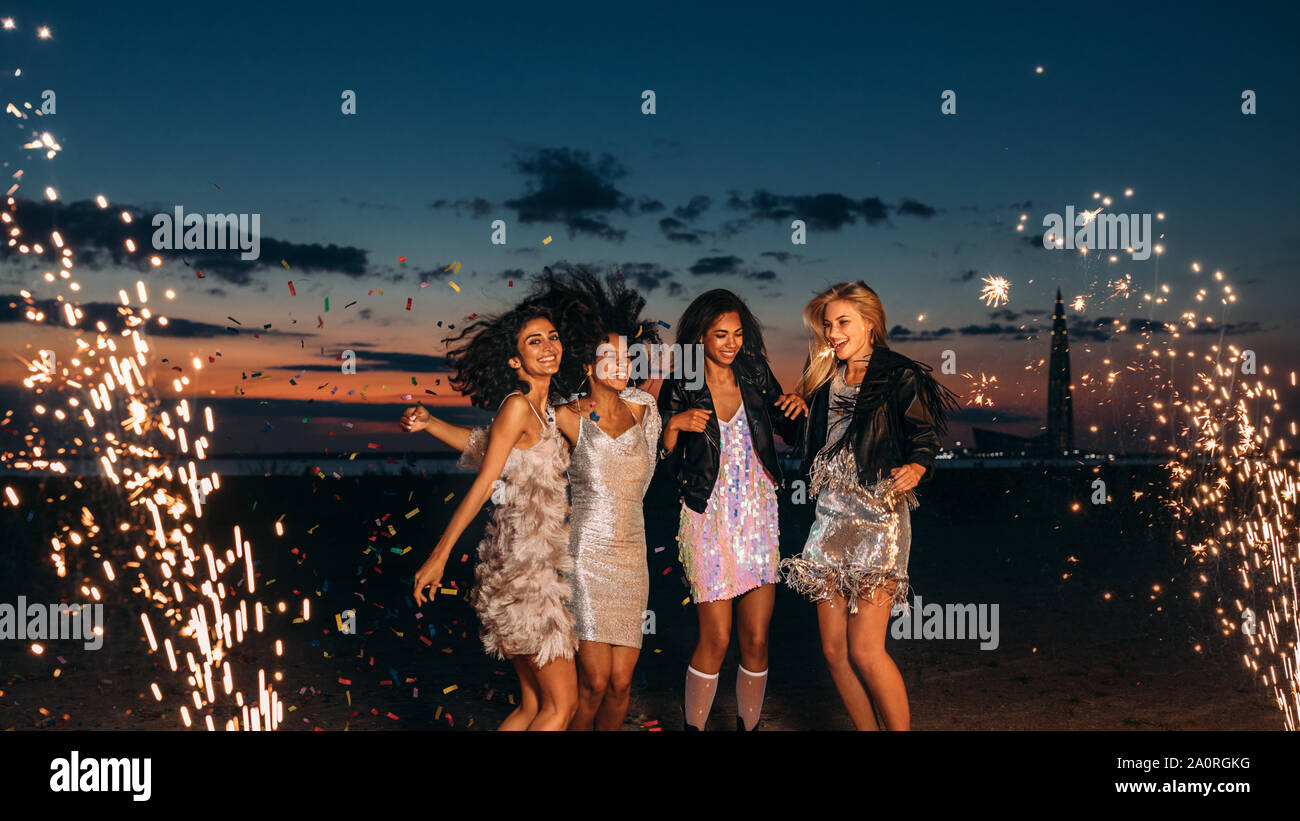Vier Frauen feiern bei Sonnenuntergang. Gerne weibliche Freunde tanzen zwischen Feuerwerk am Abend. Stockfoto