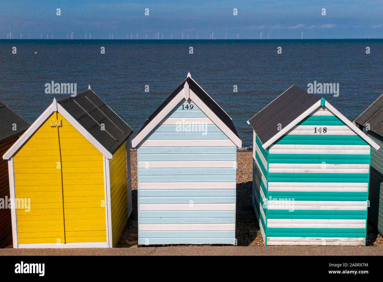 Farbenfrohe Strand Hütten in der Nähe von Whitstable an der Küste von Kent im Spätsommer mit Offshore- Windenergieanlagen im Hintergrund Stockfoto