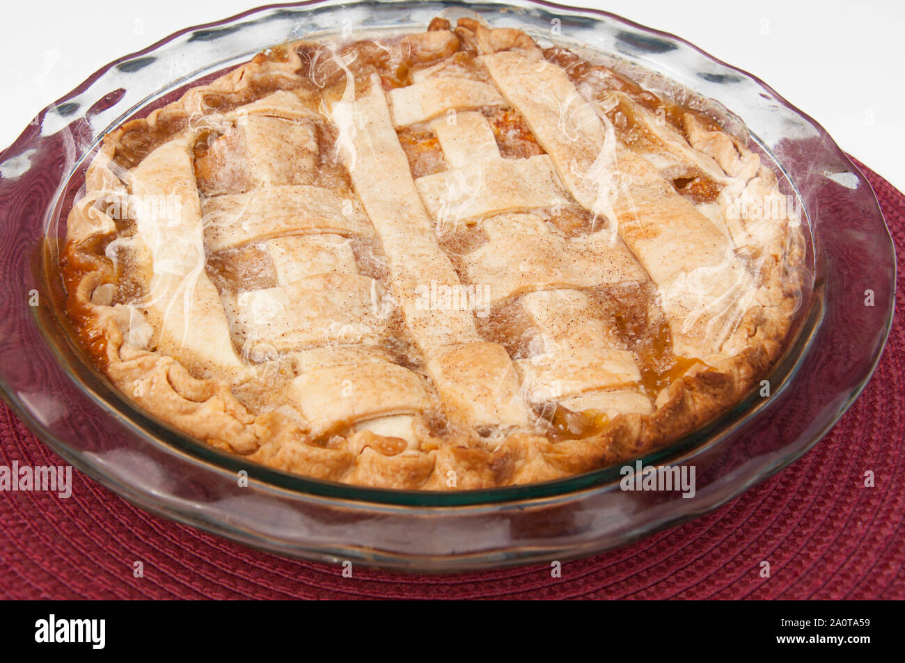 Hausgemachte peach Pie ganze uncut in einem Glas pie Pan und Burgund Unterlage. Frisch gebackene Dessert heiß aus dem Ofen mit Dampf steigt. Stockfoto