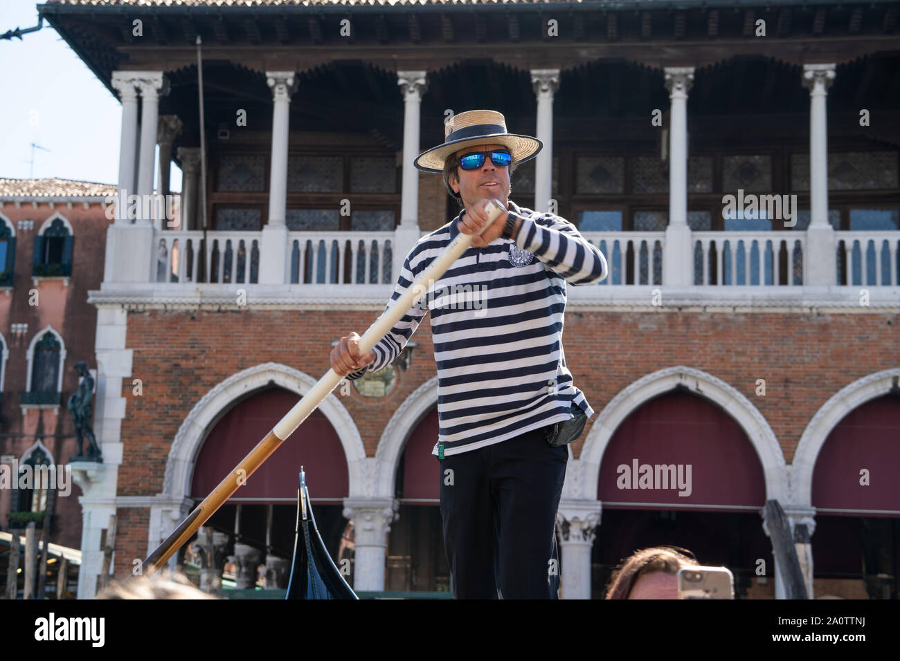 Ein gondoliere in einem traditionellen gestreiftes Hemd und Stroh Kreissäge Hut auf einer Gondel auf den Kanälen von Venedig, Italien. Tragen moderne Spiegel Sonnenbrille. Stockfoto