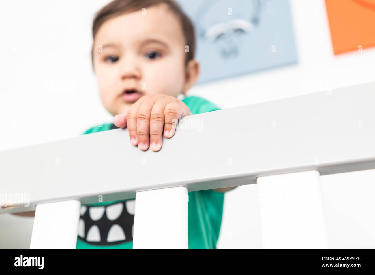 In der Nähe von Babys Hände während des Aufstehens und halten auf dem Geländer der Krippe. Das Tragen eines niedlichen grünen T-Shirt in einem hellen minimalistischen modernen nurs Stockfoto