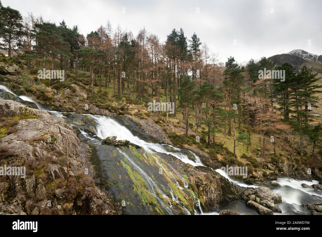 Wunderschöne Landschaft Bild der Ogwen Valley River und Wasserfälle im Winter mit schneebedeckten Bergen im Hintergrund Stockfoto