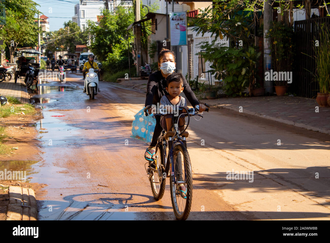 Siem Reap/Kambodscha - 25. Oktober 2018: Frau Radfahren mit ihrem Sohn sitzen auf der Quertraverse in Asien Stockfoto Siem Reap/Kambodscha - 25. Oktober 2018: Frau Radfahren mit ihrem Sohn sitzen auf der Quertraverse in Asien Stockfoto