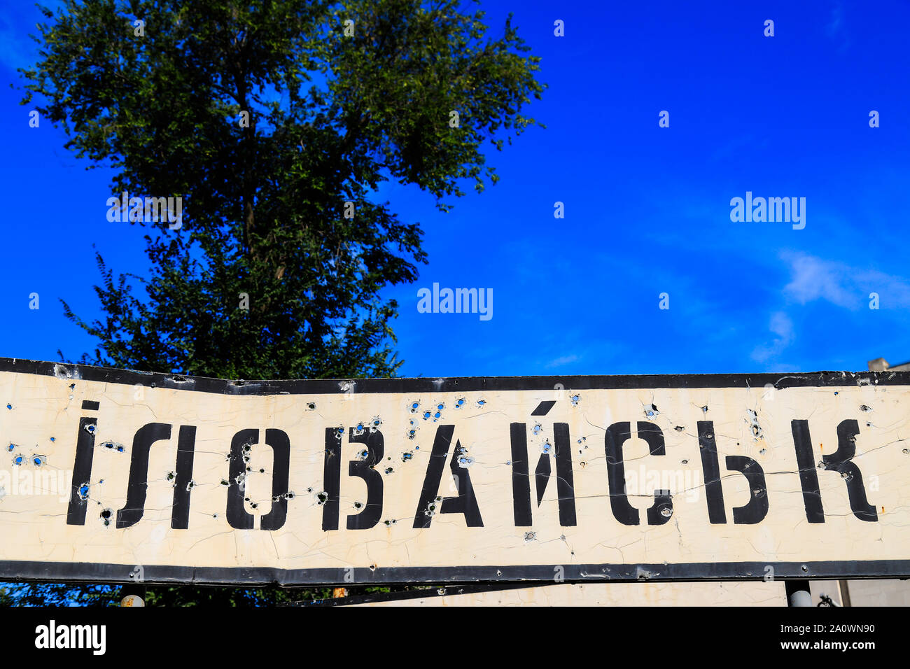 Schild mit der Inschrift in der Ukrainischen Illowaysk, der Stadt der Region Donetsk, durch Kugeln während des Krieges im Donbass, Ukraine gebrochen. Bewaffnete Stockfoto