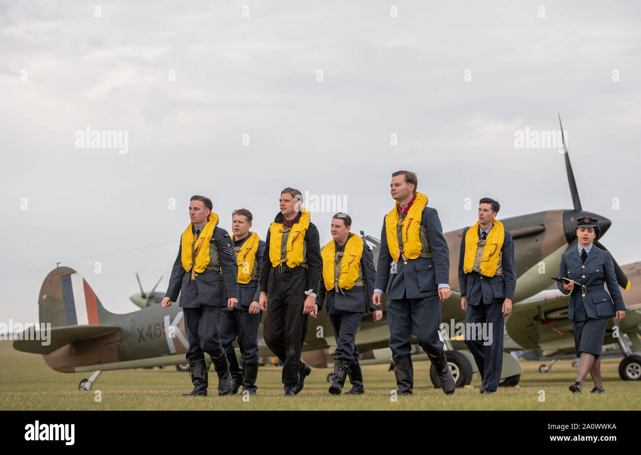 Mitglieder der historischen Reenactment Gruppe Geist von Großbritannien zu Fuß vorbei an einer Supermarine Spitfire auf der Flightline während des Duxford die Schlacht um England Air Show im Imperial War Museum in Duxford, Cambridgeshire. Stockfoto