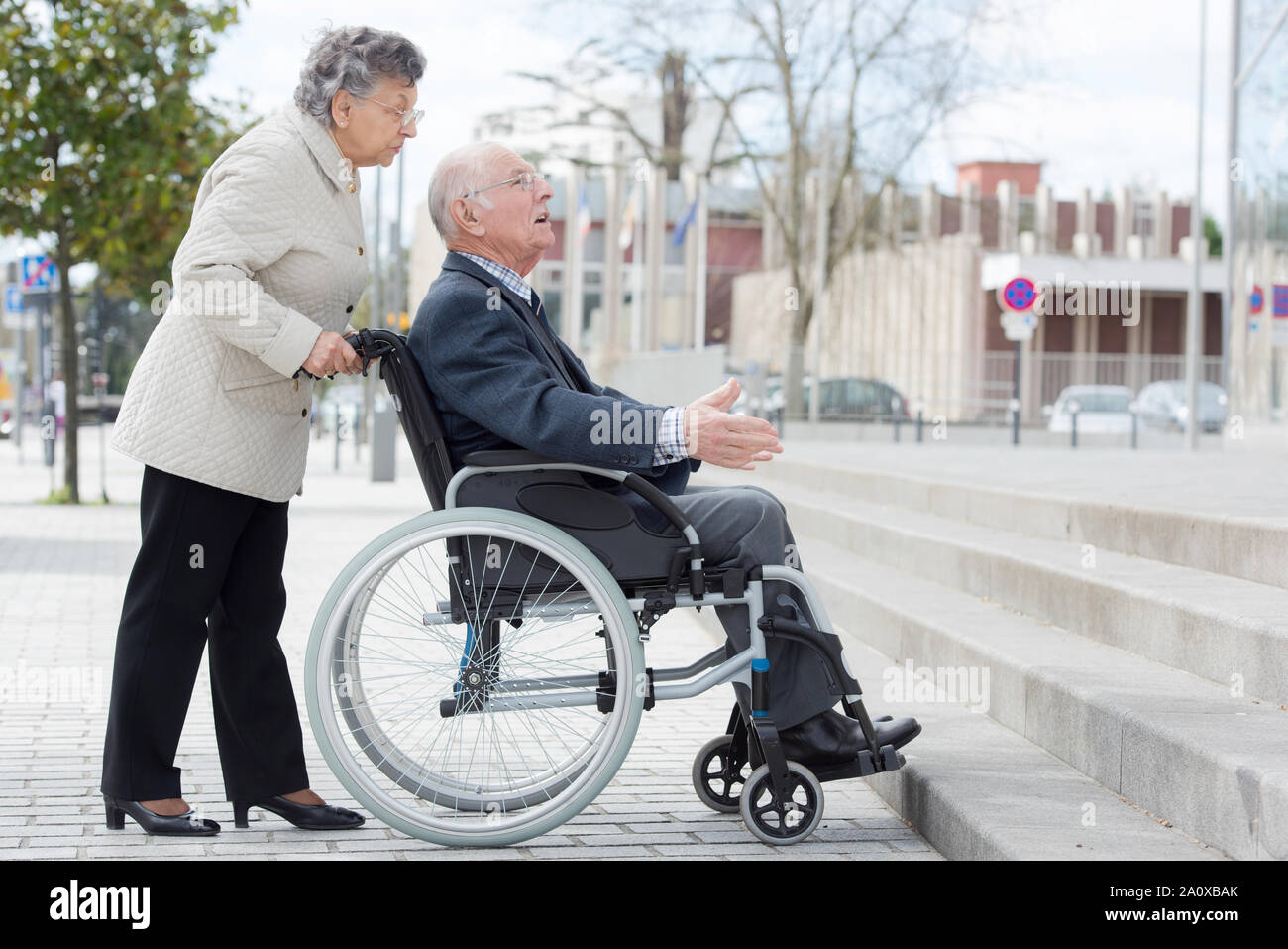 Rollstuhlfahrer und Frau vor der Treppe Barriere Stockfoto