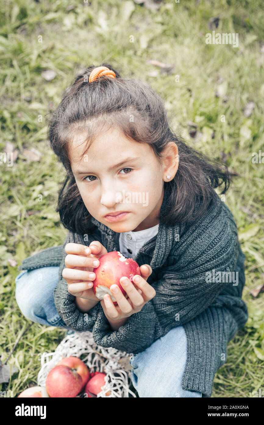 Süße Mädchen in einer grauen Jacke und Jeans frisst einen roten Apfel Stockfoto
