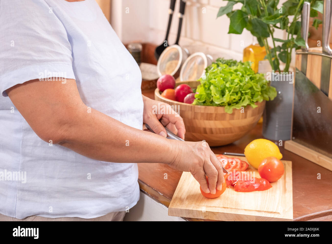 Geschlossen bis senior Hand schneiden Tomaten auf Holz Schneidebrett. Vorbereitung von Salat, gesunden Ruhestand lifestyle Konzept. Stockfoto