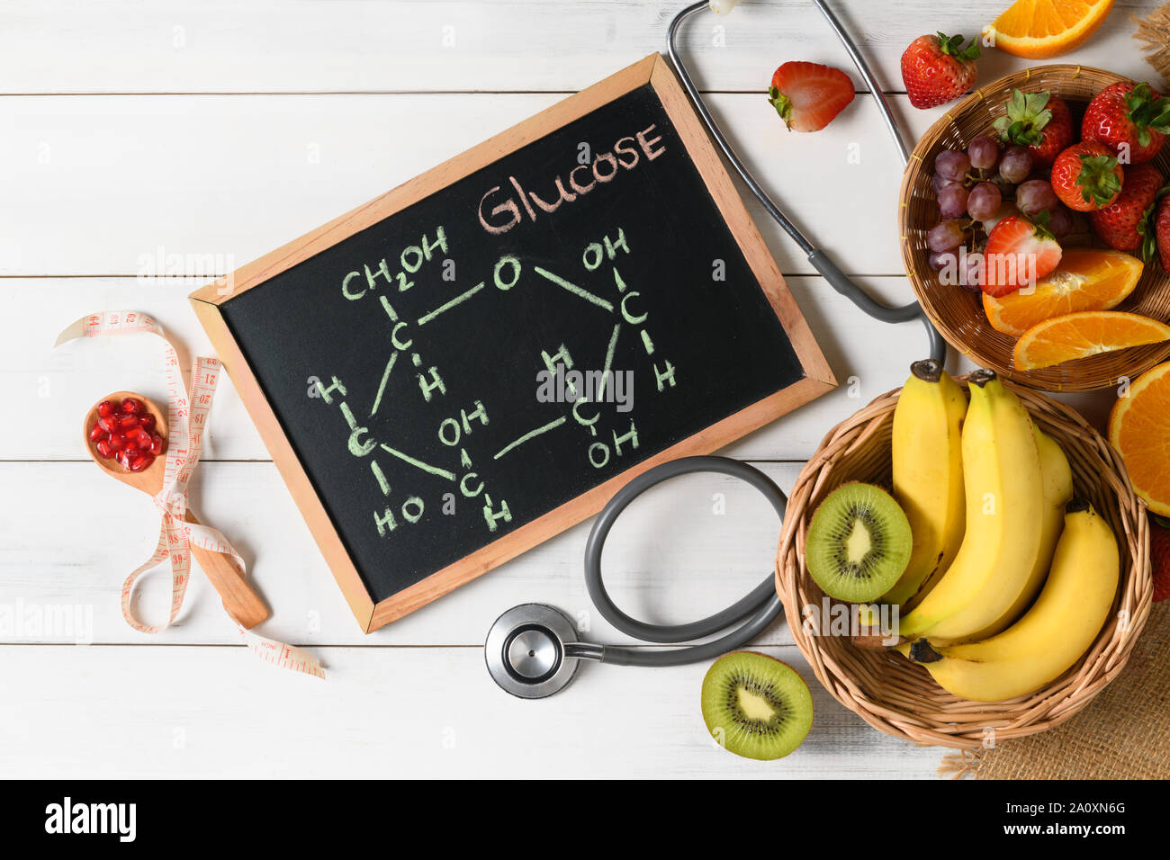 Glukosemolekül auf Tafel mit gemischten frische Früchte und Stethoskop auf hölzernen weißen Hintergrund, Ernährung und Lebensmittelkunde Konzept Stockfoto