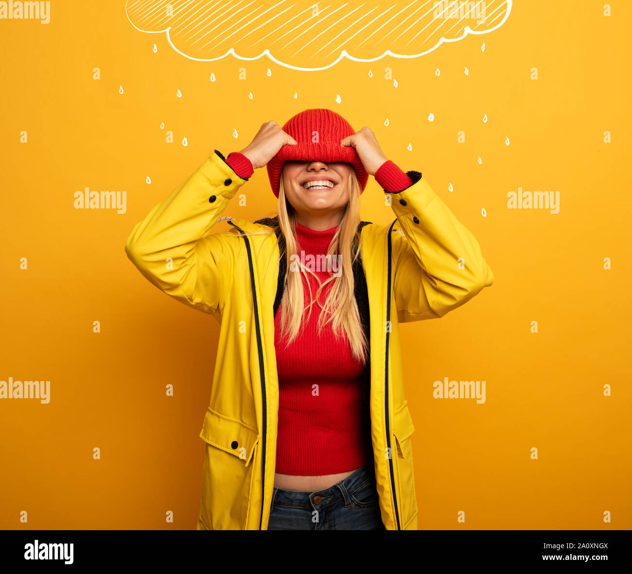 Mädchen mit Jacke auf gelben Hintergrund deckt ihr Gesicht mit ihren Hut für das Wetter Stockfoto