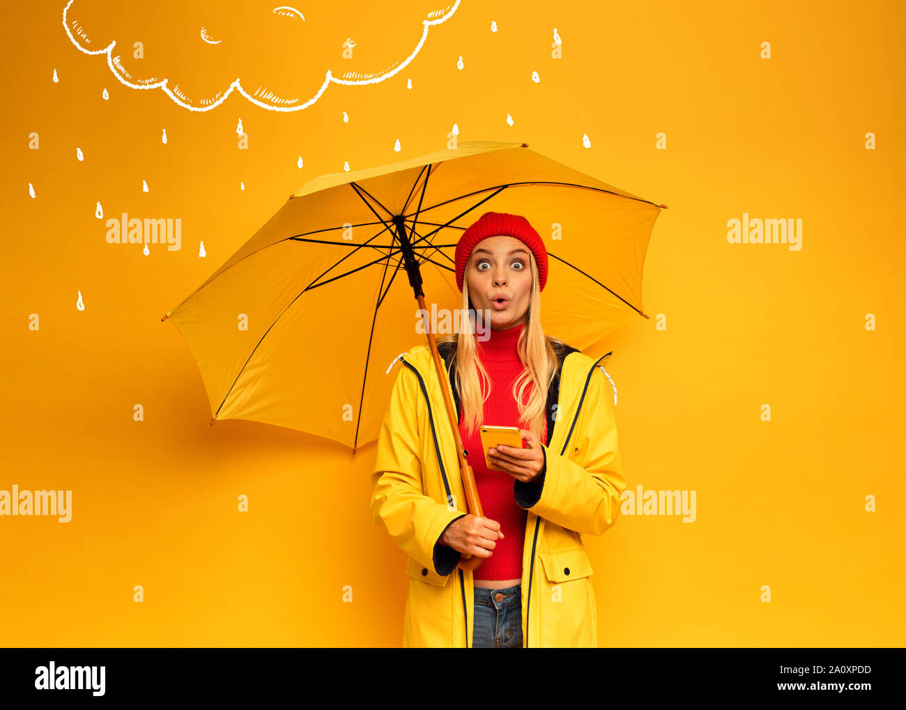 Mädchen mit Smartphone und Sonnenschirm auf gelben Hintergrund für das Wetter überrascht Stockfoto