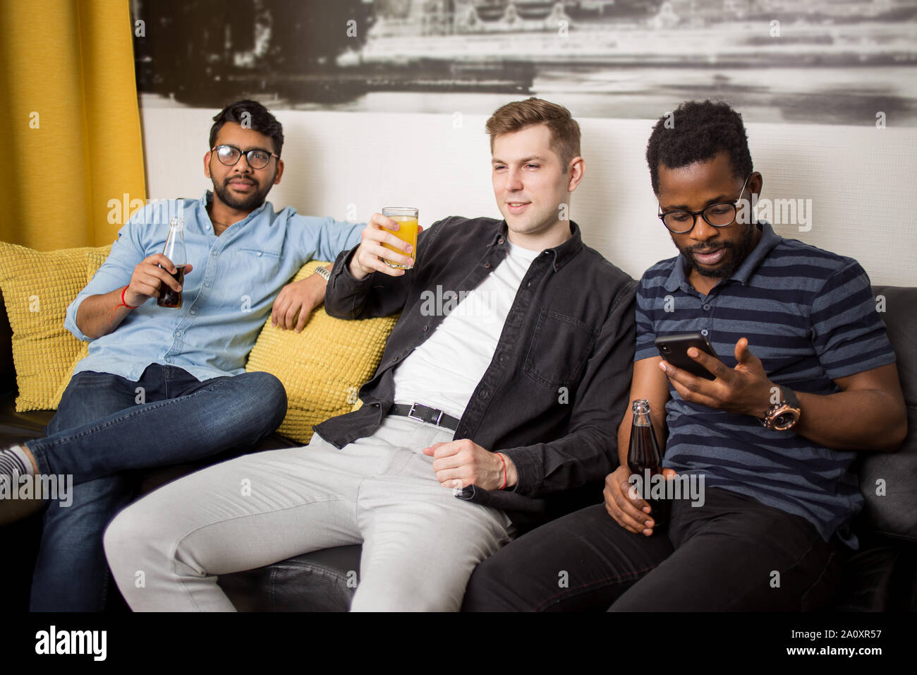 Glückliche junge Kerle Freunde ruhen zu Hause auf dem Sofa sitzen mit alkoholfreien Getränken, lächelnd dem Baseball im TV. Home Party, Sport Spiele, Freundschaft, m Stockfoto