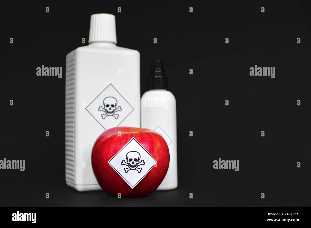 Konzept der Pestizidrückstände in landwirtschaftlichen Nahrungsmittel für den Menschen ungefährlich, zeigt ein roter Apfel und weiße Flaschen mit Gift symbol Aufkleber auf b Stockfoto