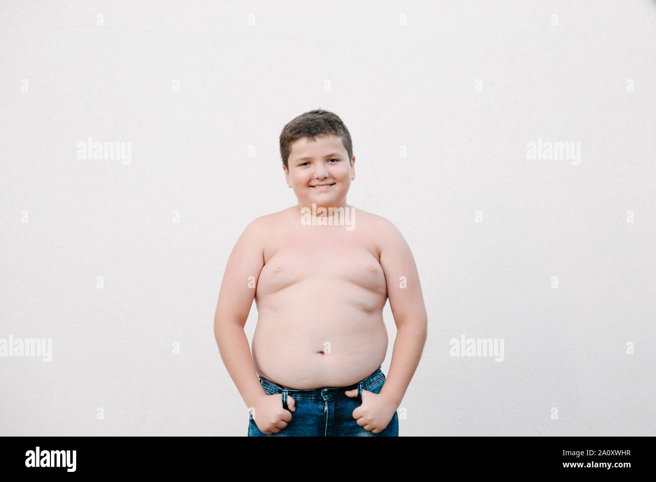 Glücklich lächelnde Fat little Kid in Jeans auf helle Wand Hintergrund mit Kopie Raum Stockfoto