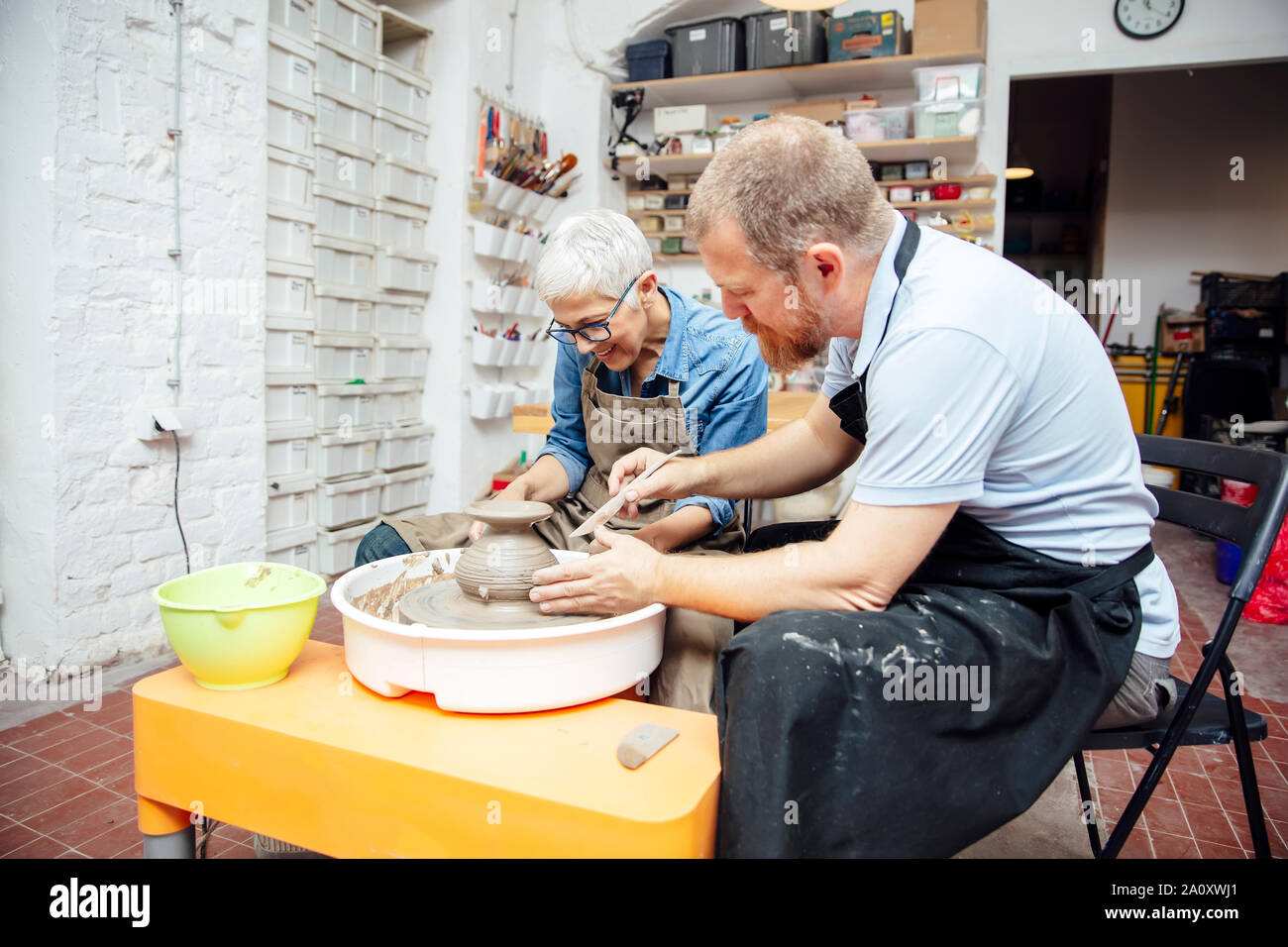 Ältere Frau spinnen Ton auf einem Rad mit Hilfe eines Lehrers an Keramik Klasse Stockfoto