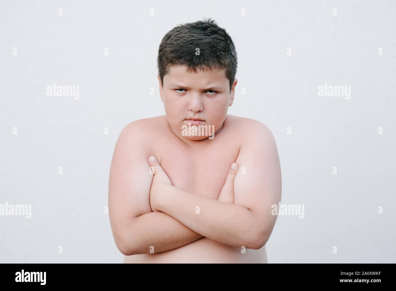 Dicken fetten kleinen Jungen mit Verärgerten Gesicht stehen auf helle Wand Stockfoto