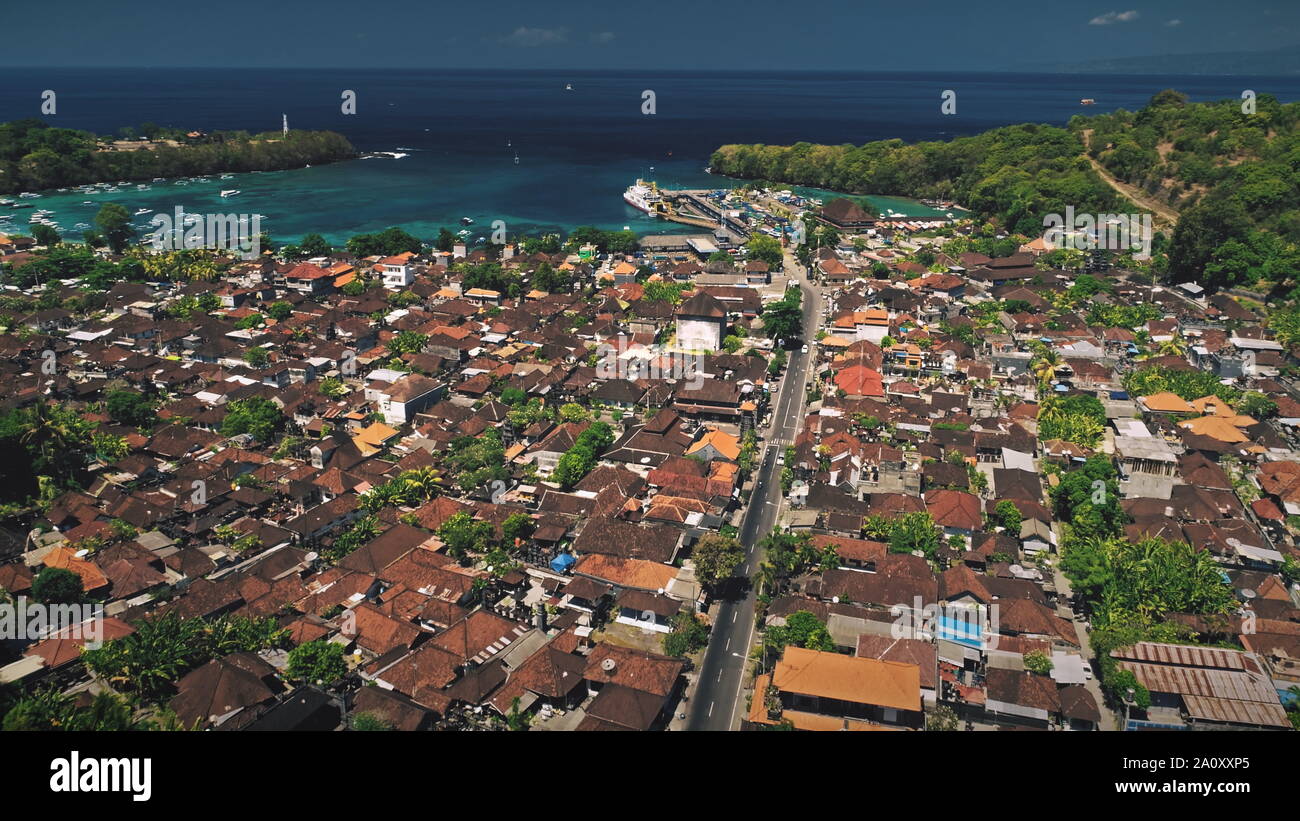 Luftbild Drohne Flug über Red Roof Häuser des Dorfes, Verkehr Straße und schönen Meer Hafen mit Fähren Pier. Erstaunliche Natur Landschaft. Tropische Insel Bali, Indonesien Stockfoto
