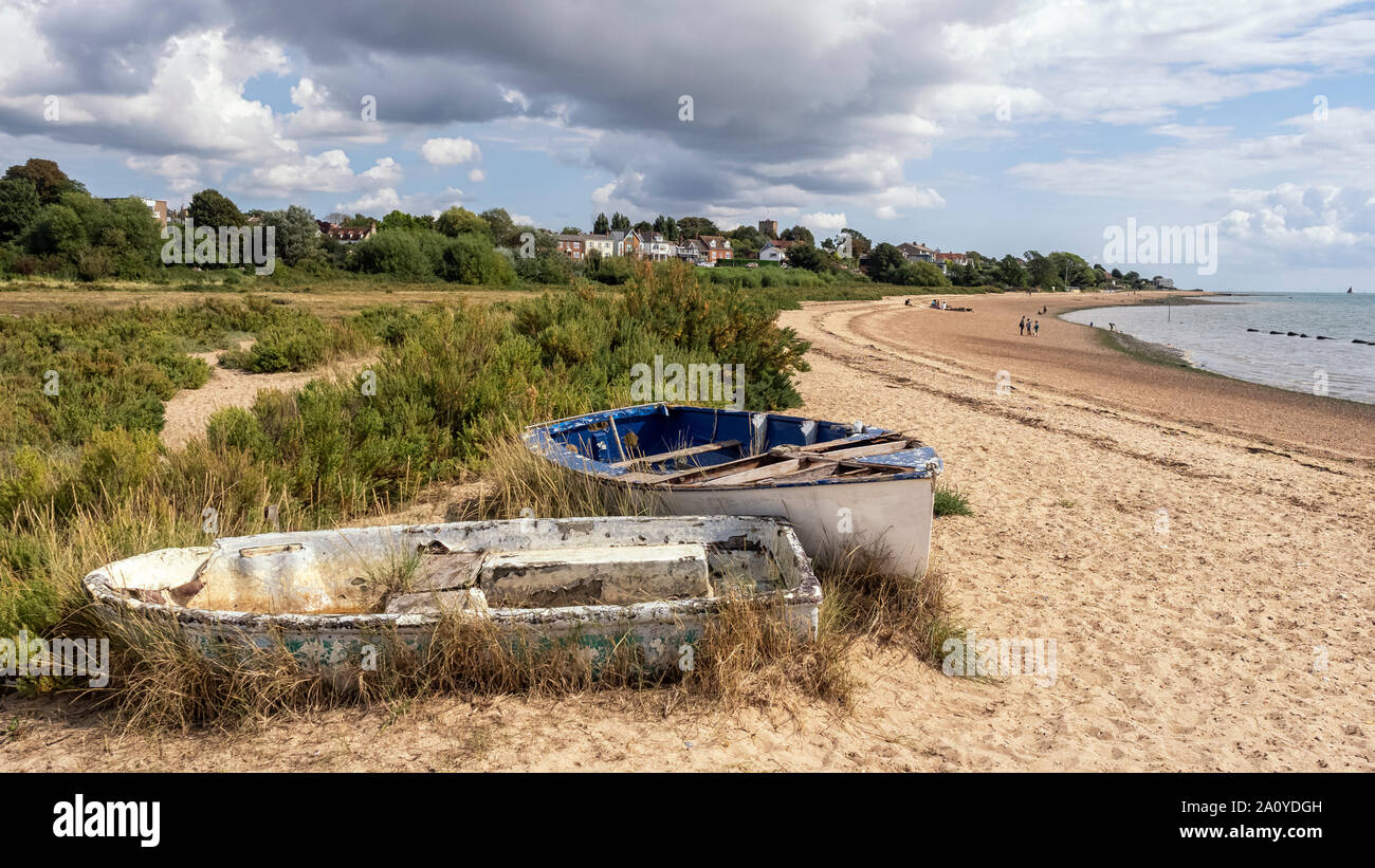 WEST MERSEA, ESSEX, Großbritannien - 31. AUGUST 2018: Der Strand entlang des Flusses Blackwater mit alten Schlauchbooten und Menschen im Hintergrund Stockfoto