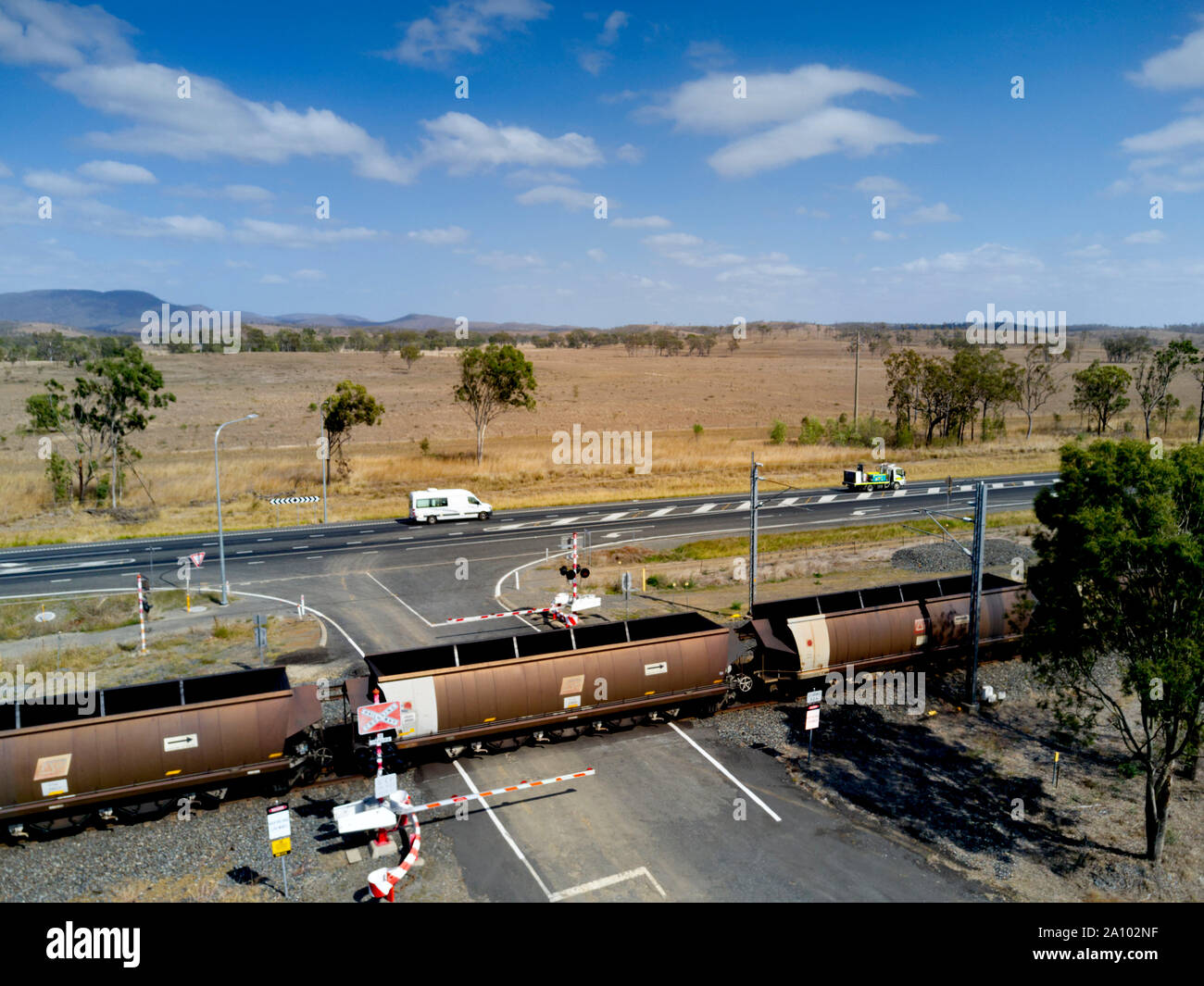 Antenne von Kohle Zug mit 106 Waggons, die durch einen Boom gesteuert Bahnübergang Position entlang der Seite des Bruce Highway nach Gladstone export Termina Stockfoto