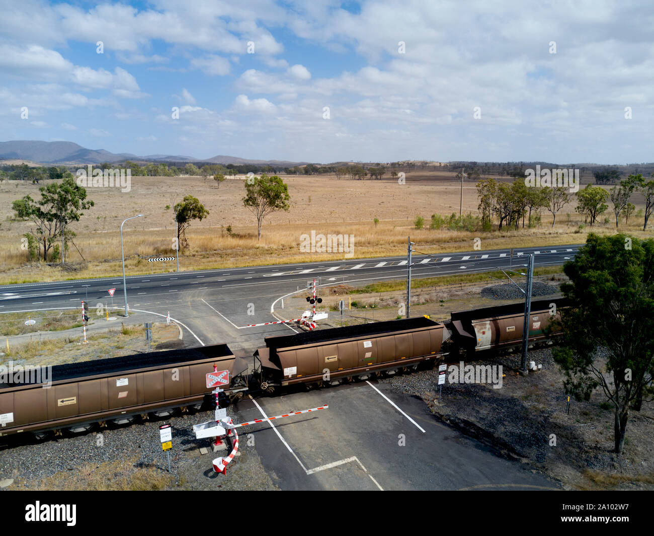 Antenne von Kohle Zug mit 106 Waggons, die durch einen Boom gesteuert Bahnübergang Position entlang der Seite des Bruce Highway nach Gladstone export Termina Stockfoto