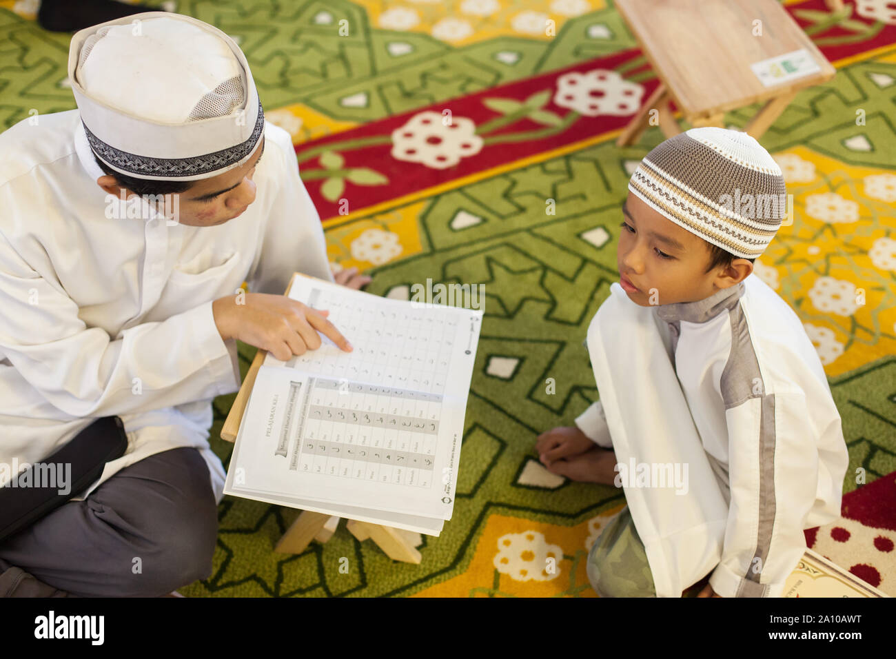 Ein Kind sitzt auf dem Teppich, von einem Lehrer unterrichtet zu Wörtern Masjid Moschee, Singapur lernen Stockfoto