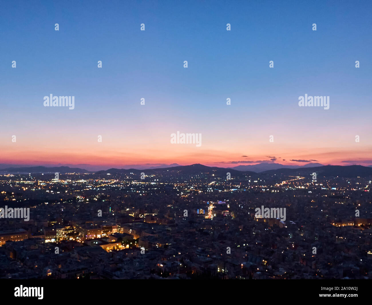 Stadt Panorama bei Sonnenuntergang. Dämmerung Landschaft mit Stadt, Berge und Wolken in den Strahlen der untergehenden Sonne. Athen, Griechenland. Stockfoto