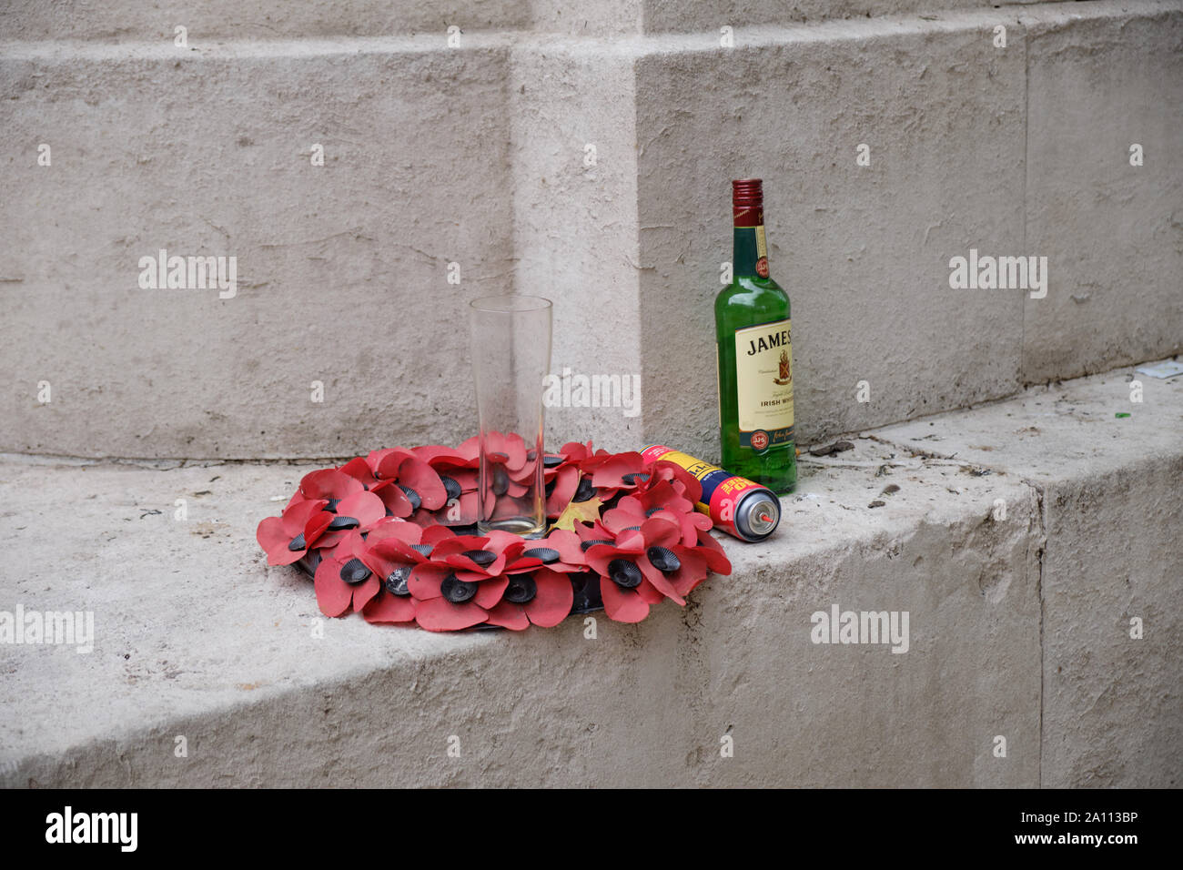 Leere Flasche Whiskey und Glas links von einem Kunststoff Mohn Kranz am Fuß der namenlosen Denkmal abgebrochen Stockfoto