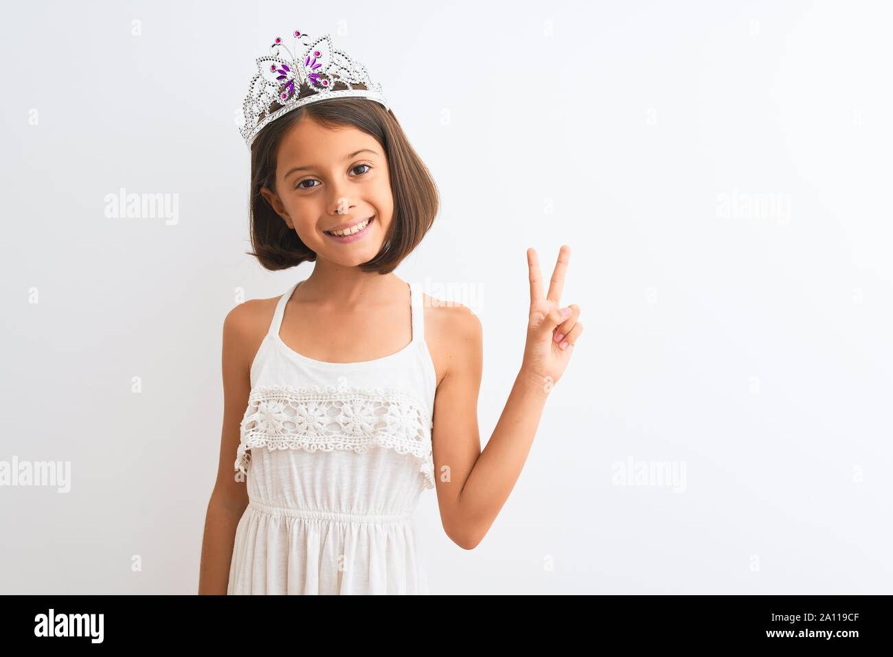 Schönes kind Mädchen mit Princess Crown stehend über isoliert weißer Hintergrund lächelnd mit glücklichen Gesicht in die Kamera winking tun Sieg unterzeichnen. Stockfoto