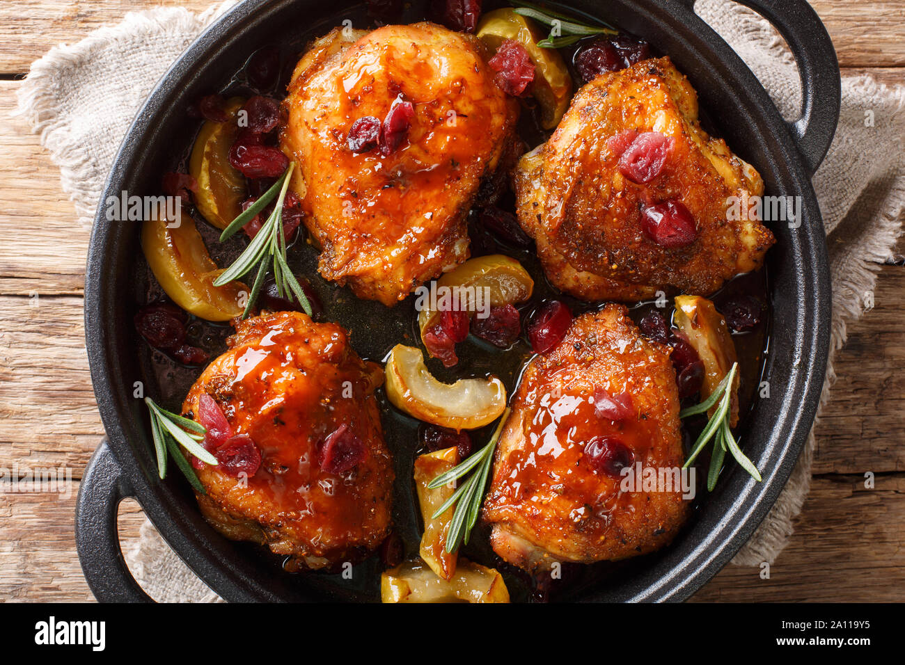 Landhausstil gebackene Hühnerkeule mit Äpfeln, Preiselbeeren und Rosmarin close-up in einer Pfanne auf dem Tisch. Horizontal oben Ansicht von oben Stockfoto